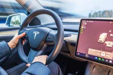 Tesla Model Y direksiyonundaki kadın ellerini otomatik pilot ekranıyla kapat ve yol trafiğini göster.