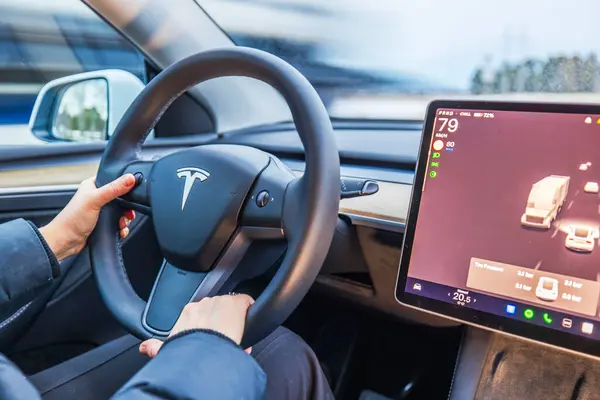 Tesla Model Y direksiyonundaki kadın ellerini otomatik pilot ekranıyla kapat ve yol trafiğini göster.