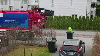 Çöp kamyonu şoförü siyah çöp tenekesini villa mahallesinin sokaklarında kol kaldırmaya bağlıyor. Uppsala. İsveç. 