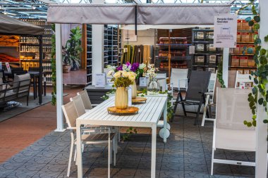 Beyaz bahçe yemek masasında çiçek vazoları ve pergola altındaki sandalyeler açık mobilya mağazasında sergileniyor. İsveç. 