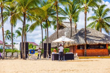 Sazlı çatılı bir sahil barı, dart tahtası oyunu ve kumlu Atlantik Okyanusu kıyısında palmiye ağaçlarının altında masaların yanında duran çalışanlar. Punta Cana. Dominik Cumhuriyeti. 