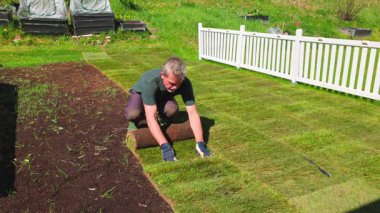 Beyaz çitin yanındaki baharda çim döşeme sırasında bir önceki bölümle yan yana çimen döşeyen adam. İsveç.