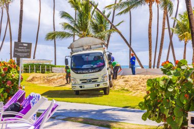 Plaj otelindeki çimlerin yanında duran işçiler. Arka planda palmiye ağaçları ve Atlantik Okyanusu var. Punta Cana. Dominik Cumhuriyeti. 
