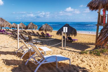 Güneşli havalarda Atlantik Okyanusu 'nun kıyısındaki altın kumun üzerindeki sazlı şemsiyelerin altında boş plaj salonları. Punta Cana. Dominik Cumhuriyeti.
