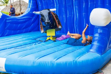 Plaj kaplamalı bir kadın tropik açık hava eğlencesi sırasında şişme mekanik boğadan düşer. Punta Cana. Dominik Cumhuriyeti. 