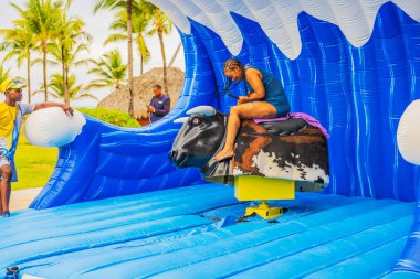 Plajdaki kadın tropikal cazibede şişme mekanik boğaya binerken konsantre oluyor. Punta Cana. Dominik Cumhuriyeti. 