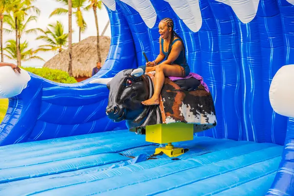 Plajdaki kadın, tropikal cazibede neşeli bir ifadeyle şişme mekanik boğaya biniyor. Punta Cana. Dominik Cumhuriyeti. 