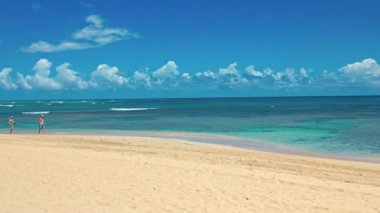 Turistler, Punta Cana 'daki Atlantik Okyanusu' nun berrak turkuaz sularında mavi gökyüzünün altında kumlu sahil boyunca yürüyorlar. Punta Cana. Dominik Cumhuriyeti. 