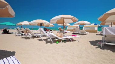 Miami 'deki zümrüt yeşili Atlantik Okyanusu' nun kumlu sahilinde şemsiyelerin altında şezlonglarda dinlenen turistler. Miami Plajı. ABD. 