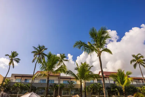 Beyaz bulutlu açık mavi gökyüzünün altında yüksek palmiye ağaçlarıyla çevrili güzel bir otel manzarası. Punta Cana. Dominik Cumhuriyeti.