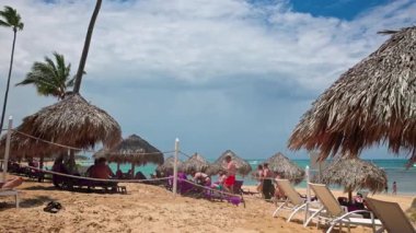 İnsanlar turkuaz Atlantik Okyanusu 'nun yakınında sazdan şemsiyeler ve palmiye ağaçlarıyla tropikal sahillerde dinleniyorlar. Dominik Cumhuriyeti. Punta Cana. 