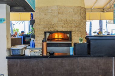 Açık hava restoranı, içinde taş pizza fırını, içinde alevler ve tezgahlar, sahil bar atmosferi. Aruba.