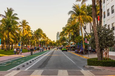 Miami Plajı 'nda Ocean Drive' da palmiye ağaçları, yürüyen insanlar, açık kafeler ve sıcak akşam ışığında arabalar. Miami Plajı. ABD. 