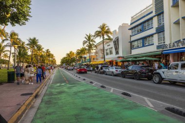Miami Beach 'te palmiye ağaçları, park edilmiş arabalar, kafeler ve yürüyen insanlarla dolu bir Ocean Drive. Miami Plajı. ABD. 