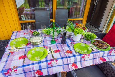 İsveç Yaz Bayramı direği, ızgara yemek, taze yeşillik ve şarap şişesiyle terasta şenlikli bir yaz masası..