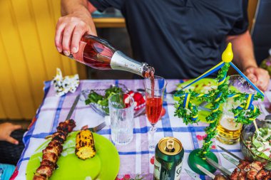 Man pouring red sparkling drink during Swedish Midsummer feast with grilled skewers, salads and fresh herbs. 