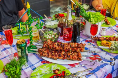 İsveç Yaz Bayramı kutlama masasında ızgara şişler, otlar, salatalar, içecekler ve şenlikli süsler. 