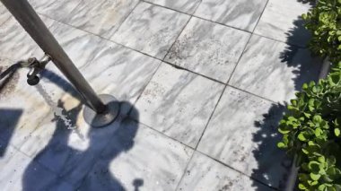 Adidas 'ta sandalet giyen biri mermer döşemedeki duş musluğunun altında ayağının altındaki kumu duruluyor. Kos. Yunanistan. 