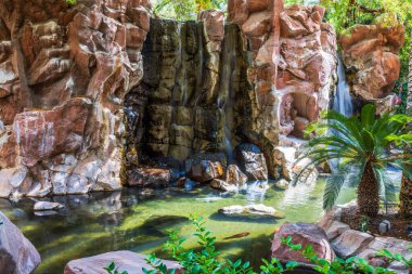 Kırmızı kayaların üzerinden akan küçük yapay şelale yeşil bitkiler ve palmiyelerle çevrili balıklarla dolu berrak bir gölete akıyor. Las Vegas mı? ABD.