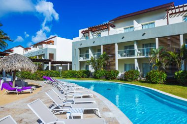 Yüzme havuzu, güneşlenme yerleri ve açık mavi gökyüzünün altında palmiye ağaçları olan lüks bir tatil köyü. Dominik Cumhuriyeti. Punta Cana. 