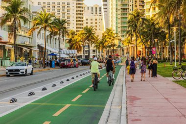 İnsanlar Miami 'de Ocean Drive boyunca palmiye ağaçları ve renkli şehir binalarıyla yürüyüp bisiklet sürüyorlar. Miami Plajı. 
