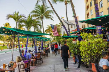 Açık oturaklı restoranlar ve Miami 'de Ocean Drive' da akşam yemeği yiyen palmiye ağaçları ve gece ışıkları olan turistler. Miami Plajı. ABD. 