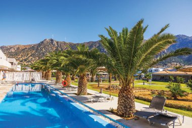 Güneşli havuz, otel bölgesinde palmiye ağaçları ve berrak mavi gökyüzünün altında dağ manzarası. Kos. Yunanistan. 