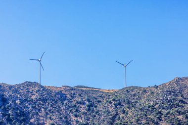 Güneşli bir günde açık mavi gökyüzünün altındaki kayalık yamaçta iki rüzgar türbini. Kos. Yunanistan.