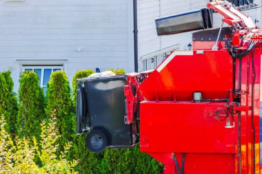 Avrupa villa bölgesinde otomatik kırmızı çöp kamyonu tarafından kaldırılan siyah çöp kutusu. İsveç.