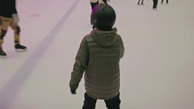 Çocuklar ve yetişkinler kırmızı boş koltuklarla kapalı buz pistinde kayıyorlar.. 