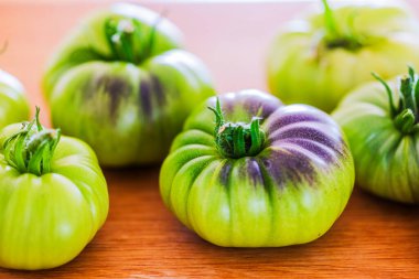 Ahşap yüzeye yerleştirilmiş mor yeşil derili olgunlaşmamış Kara Prens domateslerinin yakın görüntüsü. İsveç.