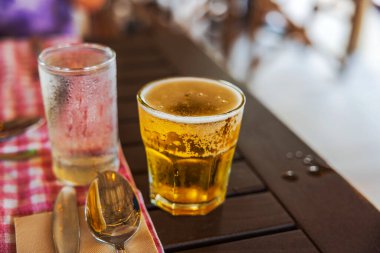 Soğuk biranın yakın görüntüsü köpüklü ve cam buharlı tahta masada kaşık ve peçeteyle. Willemstad. Curacao.