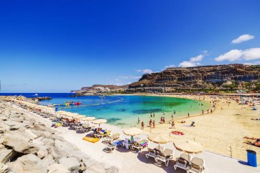 Turistler, güneş pansiyonları ve şemsiyeli Amadores Sahili turkuaz Atlantik Okyanusu koyunun arka planına karşı. İspanya. Büyük Kanarya. 