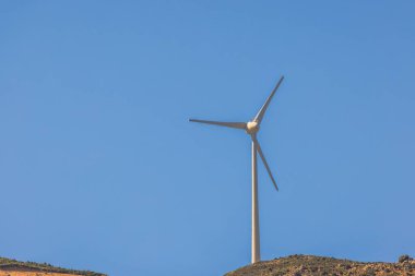 Rüzgar türbini açık mavi gökyüzüne karşı dağ yamacında duruyor güneşli havada yenilenebilir enerji üretiyor. Yunanistan. Kos.