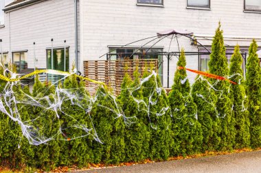 Sahte örümcek ağları ve villanın önündeki yeşil çitteki uyarı bantları ile Cadılar Bayramı dekorasyonunun güzel bir manzarası. İsveç.