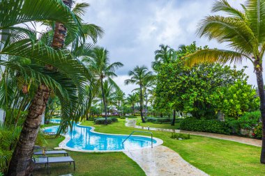 Bulutlu yağmurlu gökyüzünün altında palmiye ağaçları ve yüzme havuzu olan güzel bir tatil yeri manzarası. Punta Cana. Dominik Cumhuriyeti. 