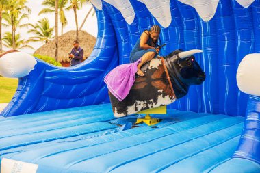 Kadınlar şişme mavi dalga çekiminde mekanik boğaya binerken tutunmaya çalışırlar. Punta Cana. Dominik Cumhuriyeti. 