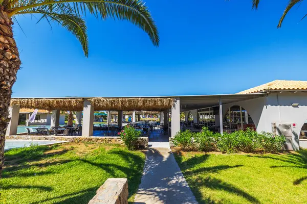 Samandan çatılı açık hava otel restoranı, masalar ve sandalyeler mavi gökyüzü arka planında palmiyelerle çevrili. Kos. Yunanistan. 