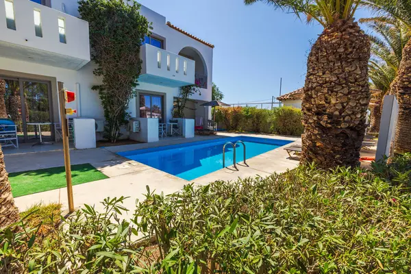 Balkonları ve palmiye ağaçları ve yeşil çalılarla çevrili özel yüzme havuzu olan bir otel binası. Kos. Yunanistan.