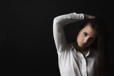 Beautiful sad girl weared in white shirt is posing on black background.
