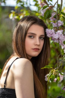 Havalı esmer kız dışarıda, Sakura ağacının yanında poz veriyor. Dikey.  