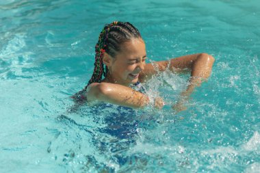 Dışarıdaki yüzme havuzunda gülümseyen uzun saçlı küçük kız oynuyor. Mutlu yaz konsepti. Yatay olarak. 