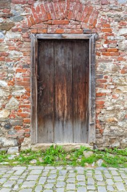 Tuğla ve taş duvar arka planında eski bir ahşap kapı. Dikey. 