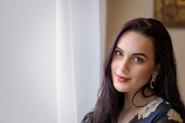 Güzel, uzun saçlı, esmer, sihirli gülüşlü kız içeride poz veriyor. Yatay olarak. 