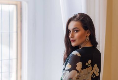 Güzel, uzun saçlı esmer kız içeride omzunun üstünden kameraya gülümsüyor. Yatay olarak.