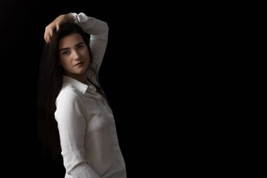 Gülümseyen esmer kız stüdyoda siyah arka planda poz veriyor. Yatay olarak. 