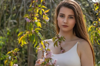 Havalı esmer kız açık havada, Sakura ağacının yanında poz veriyor. Yatay olarak. 