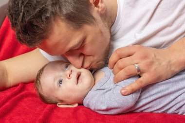 Genç baba yeni doğmuş bebeğini öpüyor. Yatay olarak. 