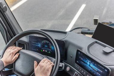 Sürücü ellerinin yüksek açılı görüntüsü, direksiyon simidi ve hareket halindeki bir kamyonun kabinindeki modern gösterge paneli. Yatay olarak. Tüm potansiyel markalar kaldırıldı. 