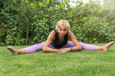 Esnek, gülümseyen olgun bir kadın dışarıda bacaklarını ayırıyor. Yatay olarak. 